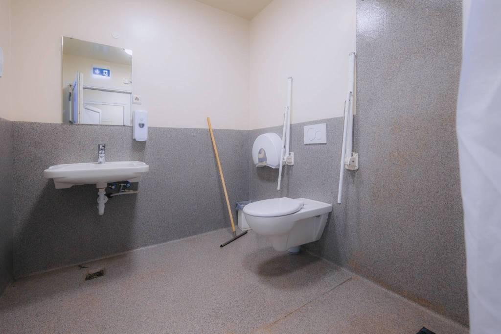 Accessible bathroom with grab bars beside the toilet, a wall-mounted sink, a mirror, and a broom.