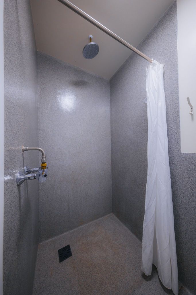 A simple shower area with gray stone walls and floor, featuring a silver showerhead and a white curtain on a rod.
