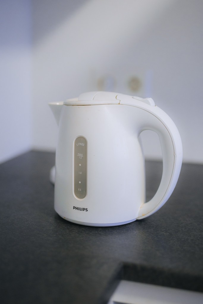A white electric kettle with a smooth design sits on a dark countertop. It's simple and modern, with measurement markings on the side.