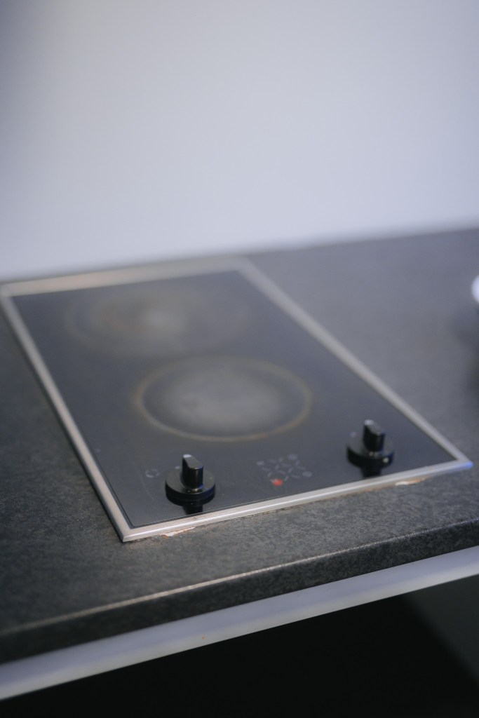 Close-up of a sleek black induction cooktop with two burners and two control knobs on a dark countertop.