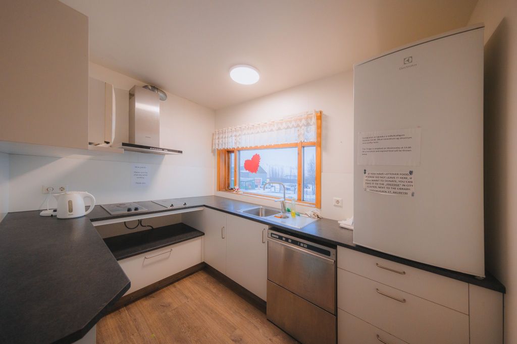 Modern kitchen with white cabinets, black countertops, and wood floor. A large fridge is on the right, with a heart-shaped sticker on the window.