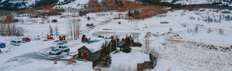 Snow-covered landscape with scattered buildings, vehicles, and evergreen trees.