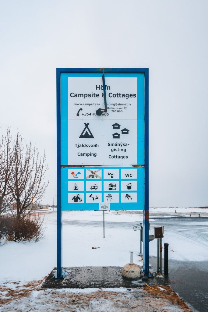 Sign for Höfn Campsite & Cottages with icons for amenities like WiFi, WC, and charging.