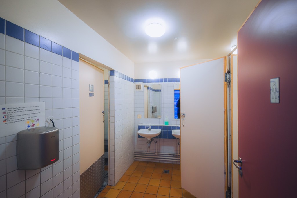 Public restroom with white and blue tiles. Open stall doors reveal sinks and mirrors.