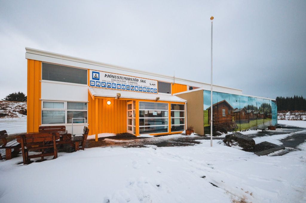 A bright yellow and white building stands in a snowy landscape. It features a large sign and a mural of houses. Wooden benches adorn the entrance.