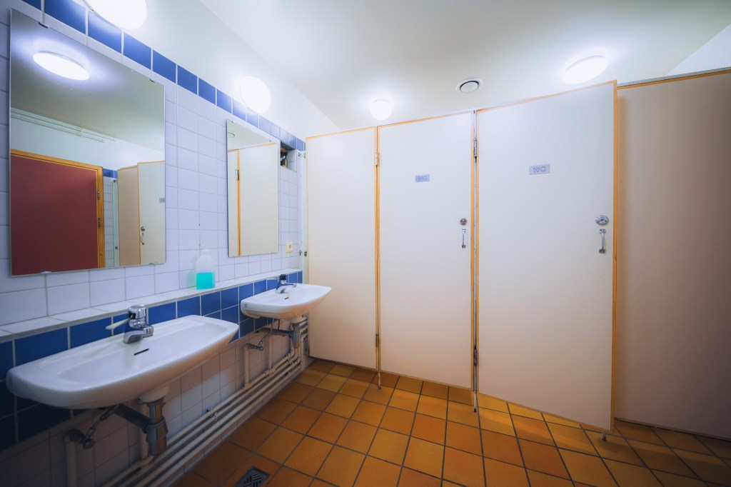 Restroom with blue-tiled walls, two sinks, mirrors, and three white stall doors.