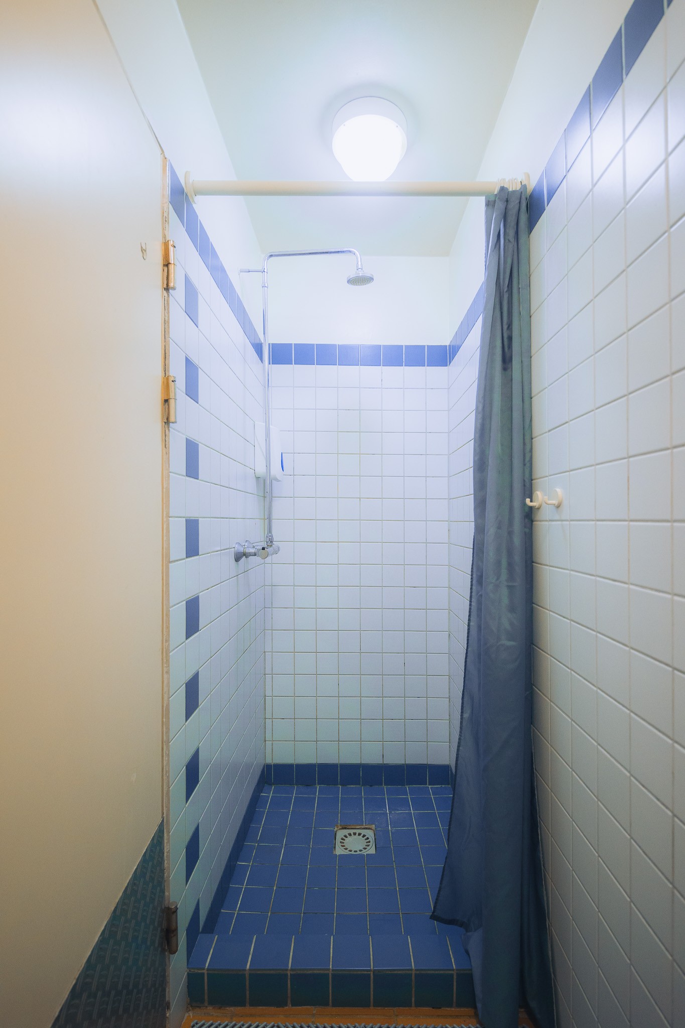 Shower stall with a blue and white tiled design, featuring a curtain on the right, overhead light, and a simple showerhead.