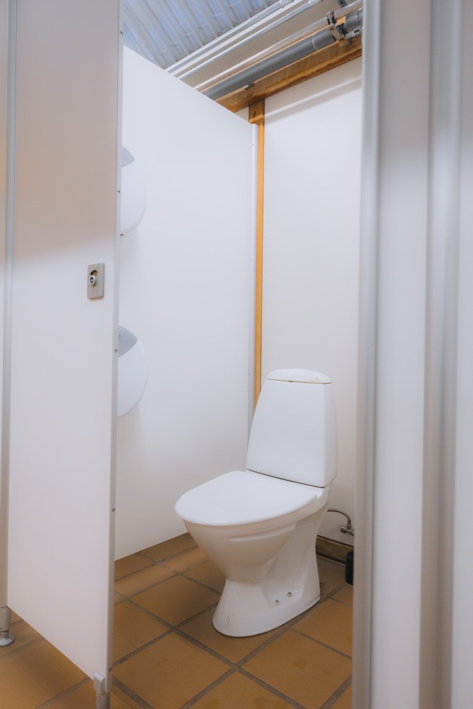 A clean, white toilet in a public restroom stall with tiled floors and white partitions.