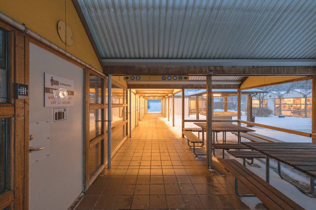 Covered walkway with wooden benches on a snowy day, warmly lit leading to a bright end.