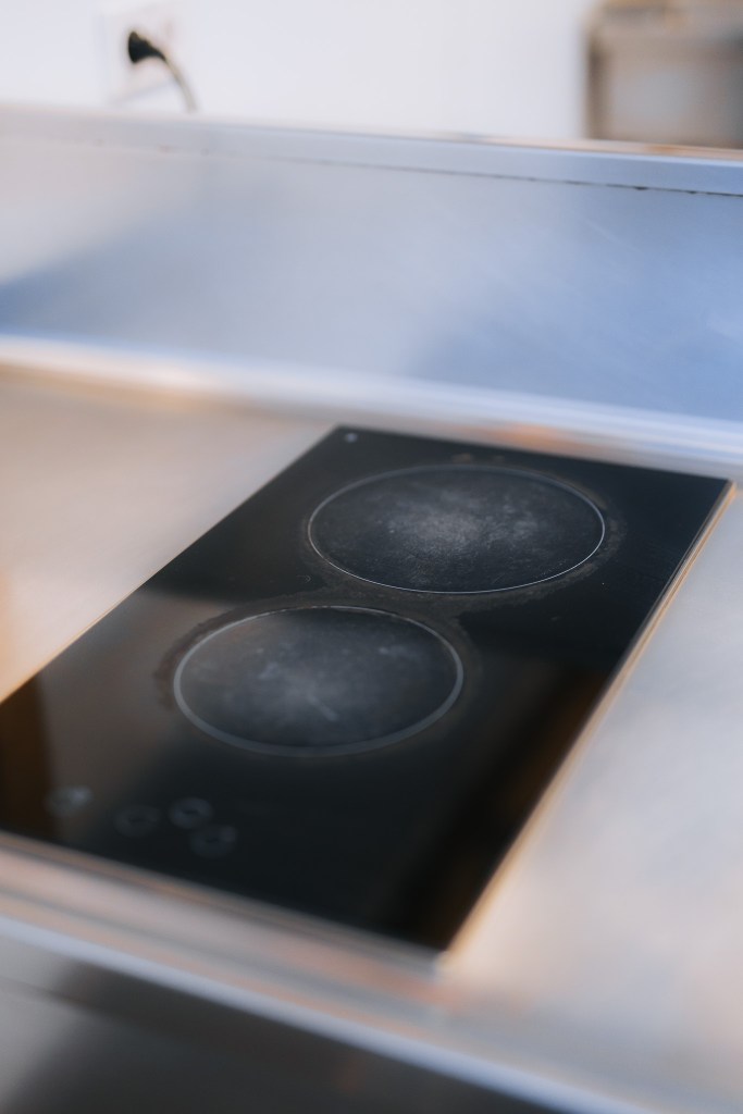 A sleek, black induction cooktop with two burners is embedded in a reflective metal surface.
