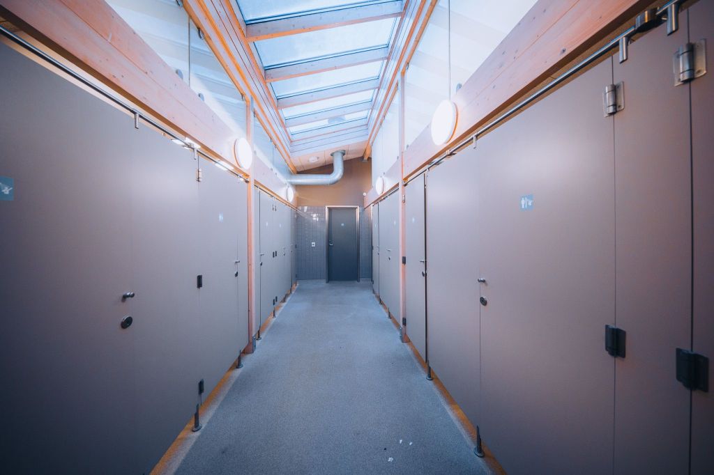 A narrow corridor with light gray walls and doors, illuminated by round ceiling lights and skylights.
