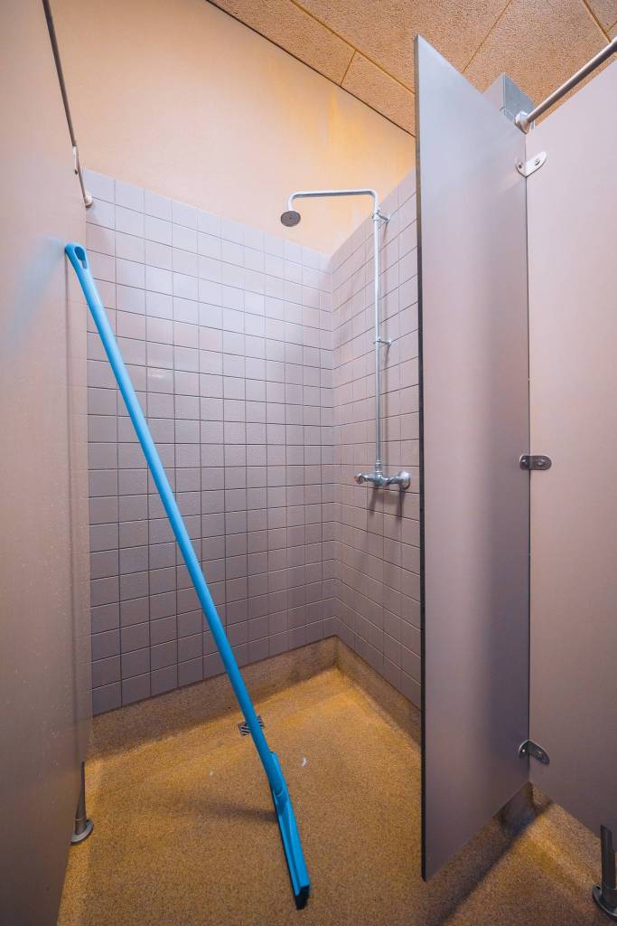 Shower stall with gray tiles and a blue mop leaning inside. The door is partially open.
