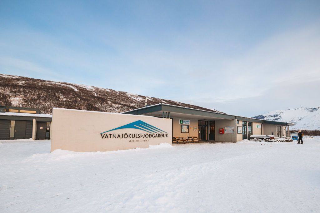 Snow-covered visitor center at Vatnajökull National Park in Iceland, set against a backdrop of snowy mountains under a clear, pale blue sky.