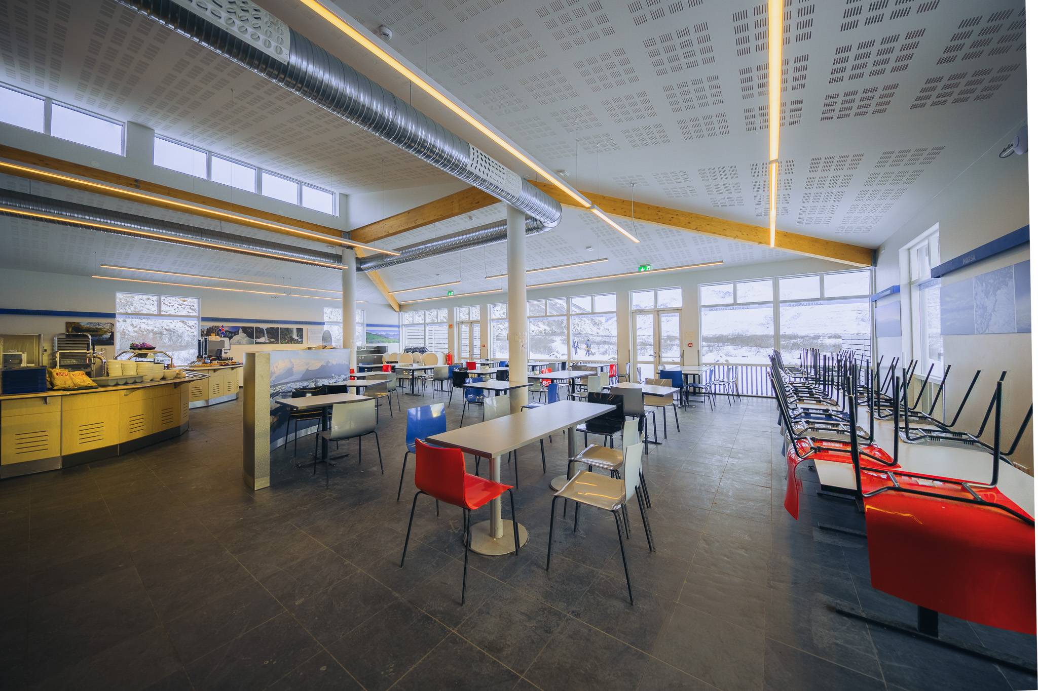 Spacious, modern cafeteria with colorful chairs, sleek tables, and large windows. Chairs are stacked on tables.