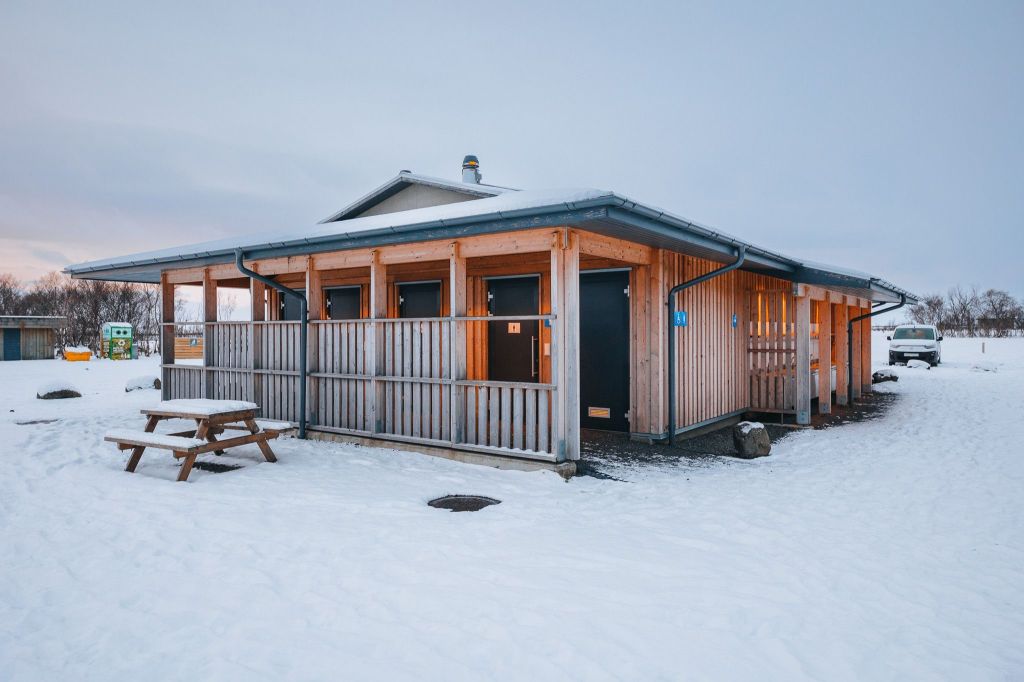 Wooden cabin with a wrap-around porch, set in a snowy landscape.