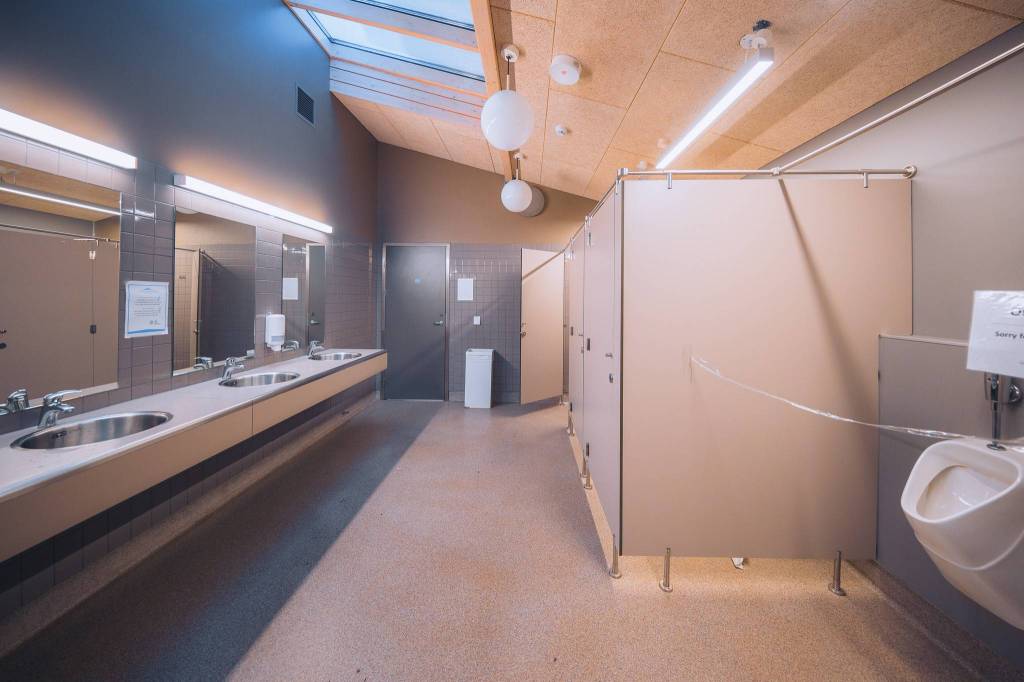 Wide-angle view of a clean, modern bathroom with skylight. Features mirrors, sinks, stalls, and a urinal.
