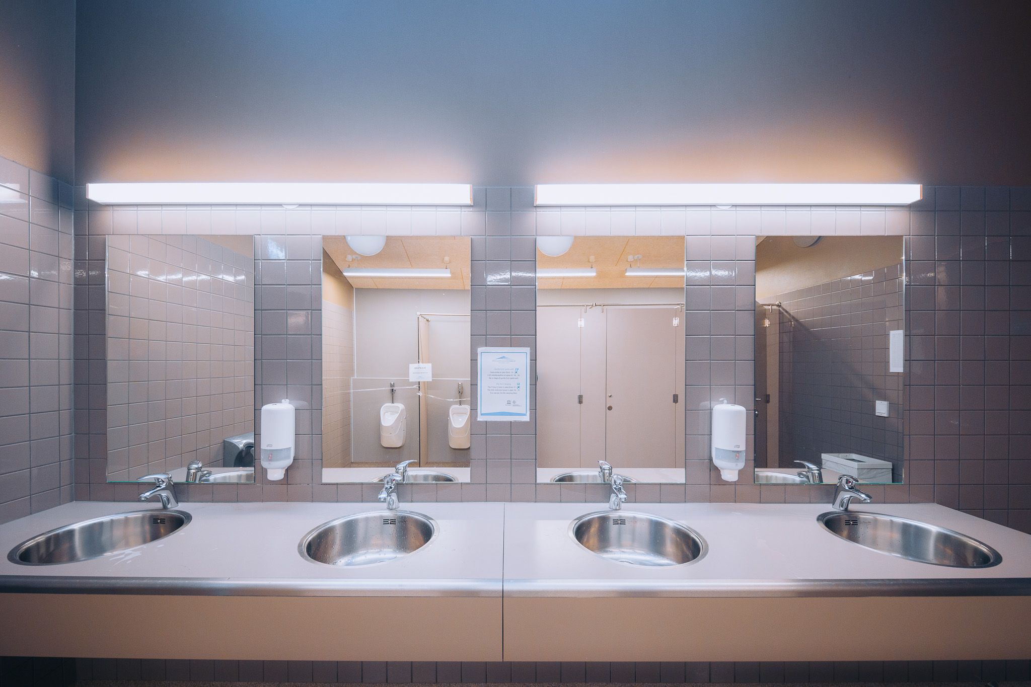 A modern public restroom with stainless steel sinks and rectangular mirrors.
