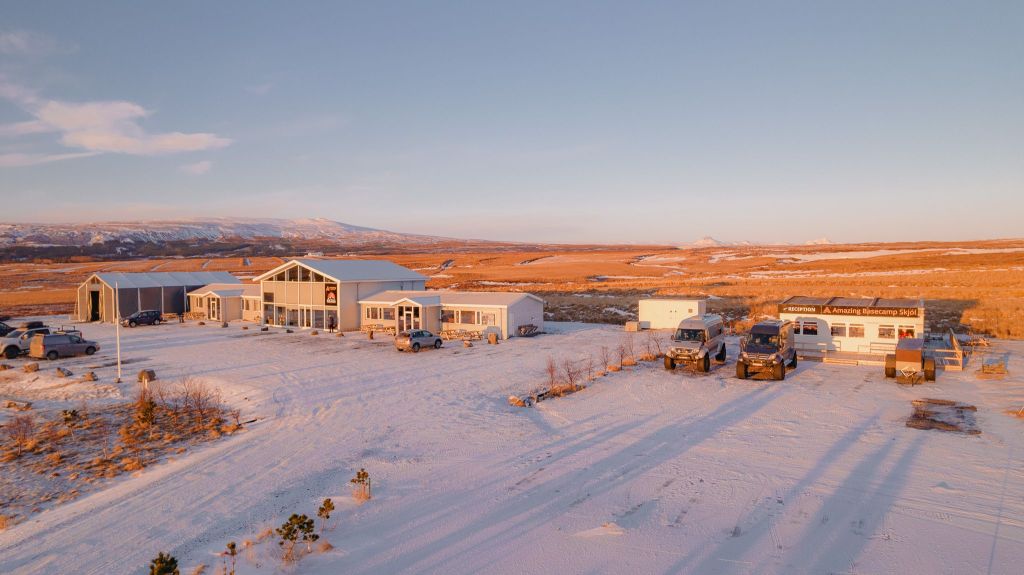 A snowy landscape at sunrise featuring a cluster of buildings, vehicles, and a sign for a restaurant.