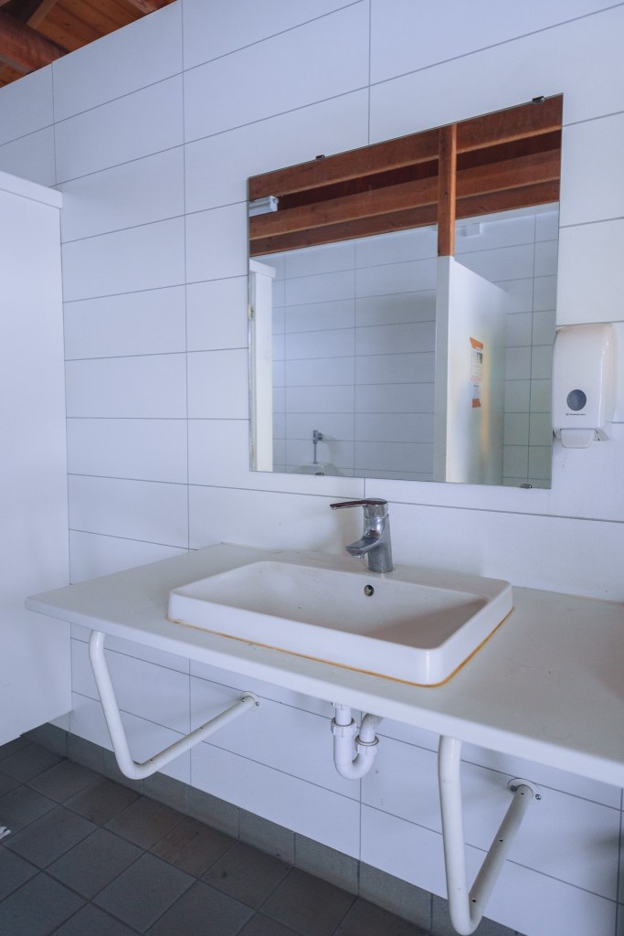 A clean, white bathroom sink with a rectangular mirror and soap dispenser on a tiled wall.