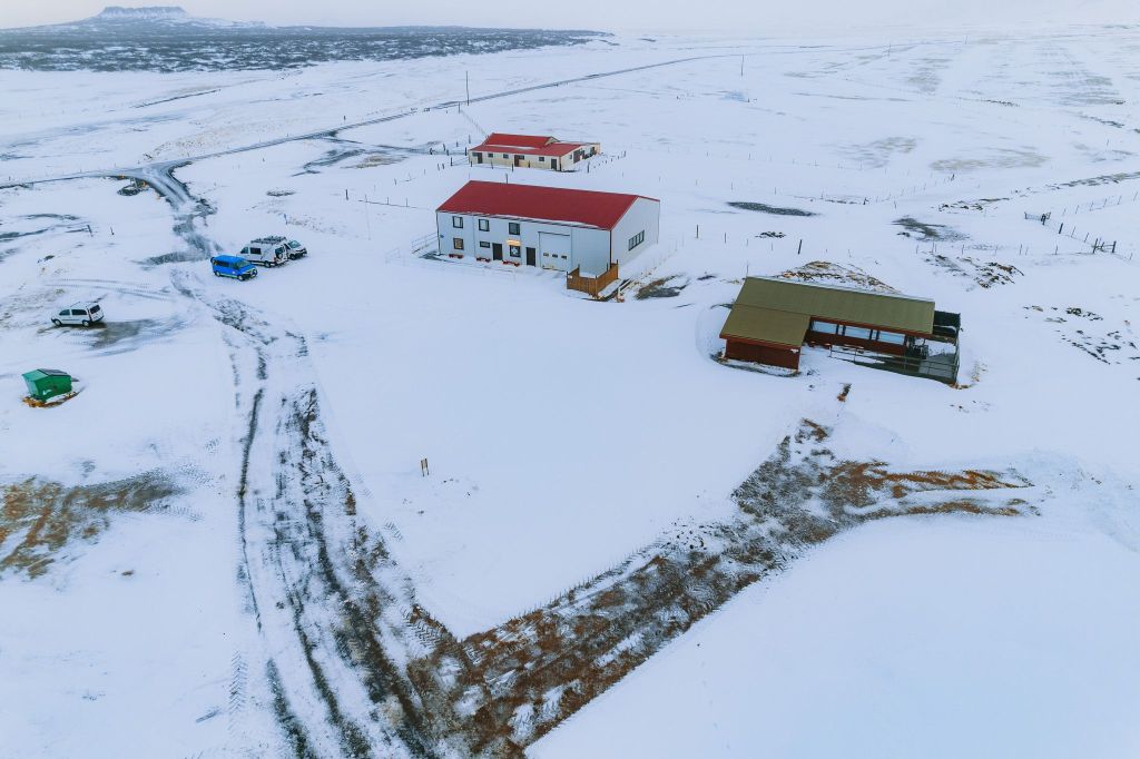Snowy landscape with a few buildings featuring red roofs. Vehicles are parked nearby.