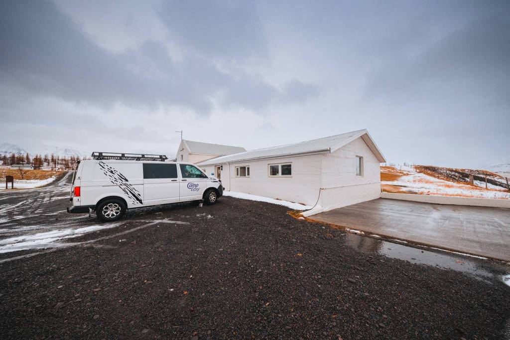 A white van parked outside a small white building on a snowy driveway.