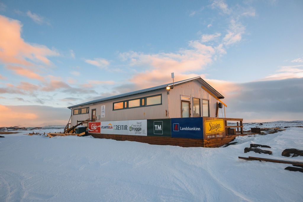 A small building on a snowy landscape, adorned with colorful sponsor banners.