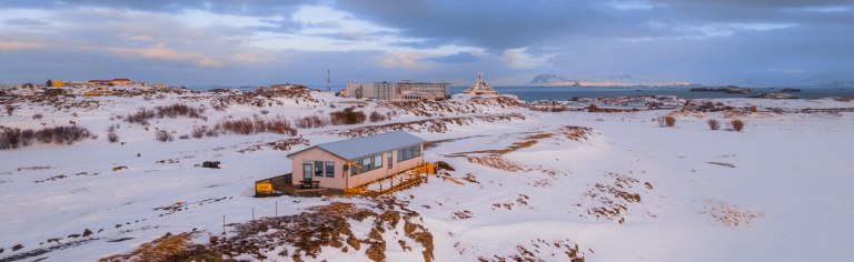 Snowy Icelandic landscape with distant buildings, a prominent domed structure, and ocean in the background.