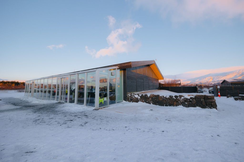 Modern building with large glass windows sits in a snowy landscape under a clear blue sky.