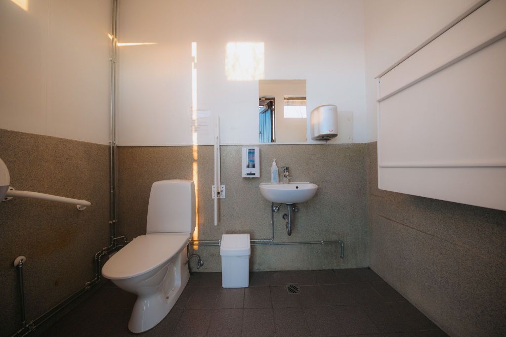 A clean, minimalist bathroom with a toilet, small sink, mirror, and dispenser.