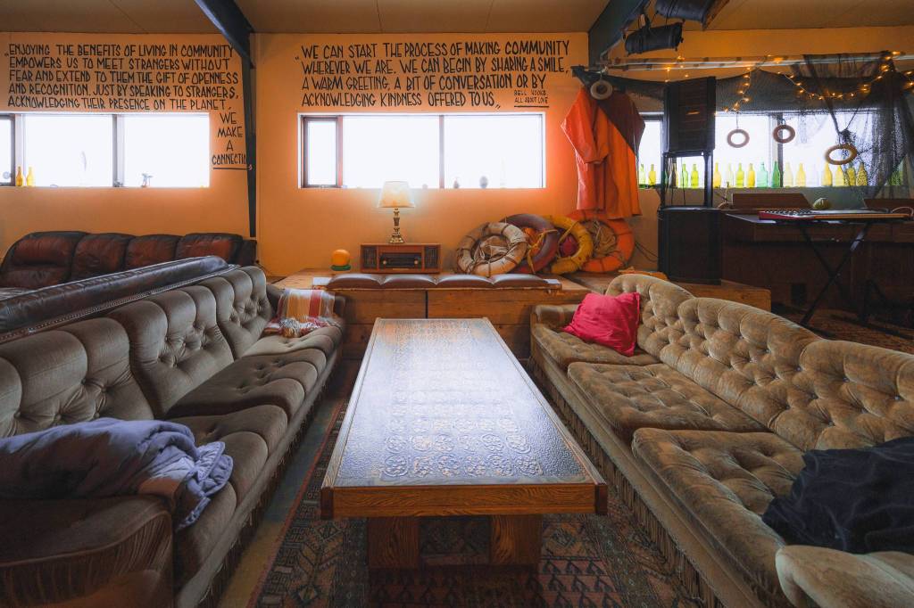 Cozy room with vintage sofas and a carved wooden coffee table. Warm lighting, pillows, and wall quotes.