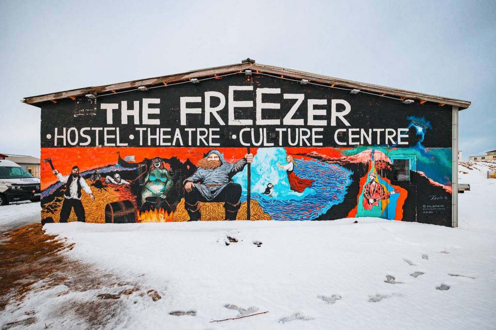 Colorful mural on the side of The Freezer Hostel, Theatre, Culture Centre, featuring vibrant, imaginative characters and landscapes against a snowy backdrop.
