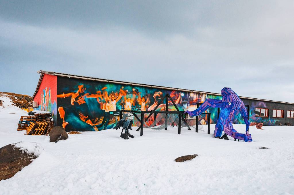 A colorful mural featuring cheering athletes adorns a long building against a snowy landscape.