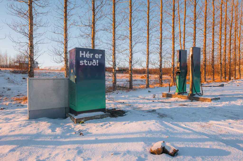 Electric charging station covered in snow with a backdrop of bare trees under a clear sky.