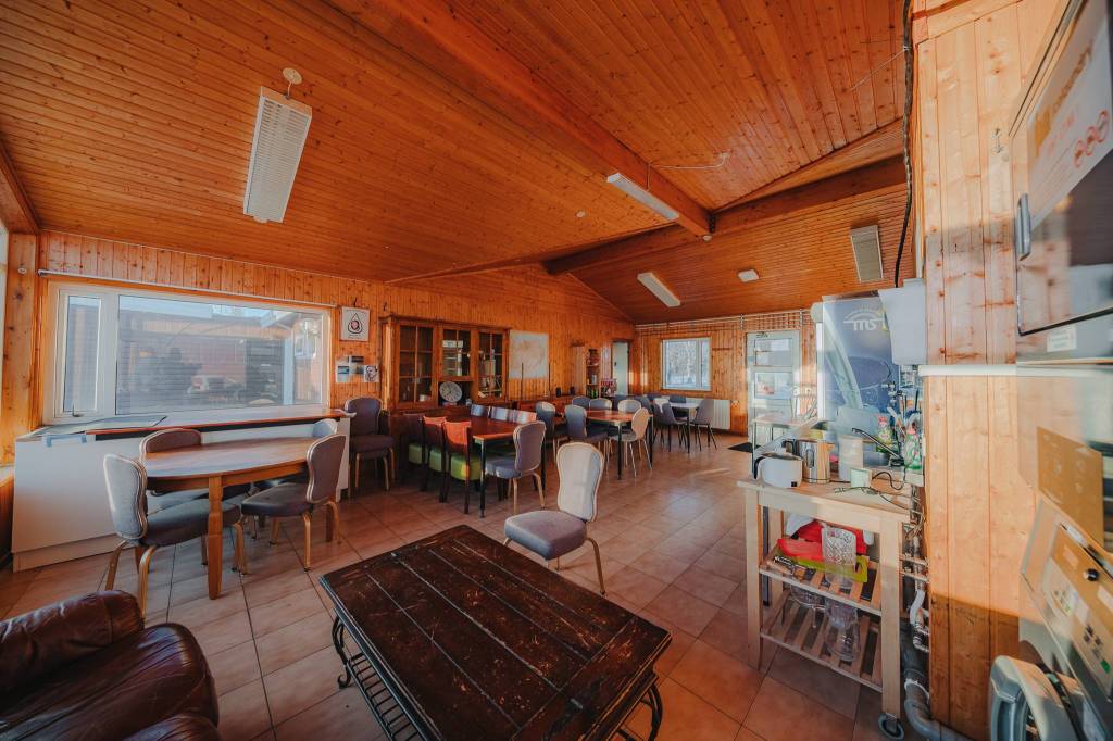 A spacious wooden interior with a high ceiling and large windows. Multiple tables and chairs fill the room.