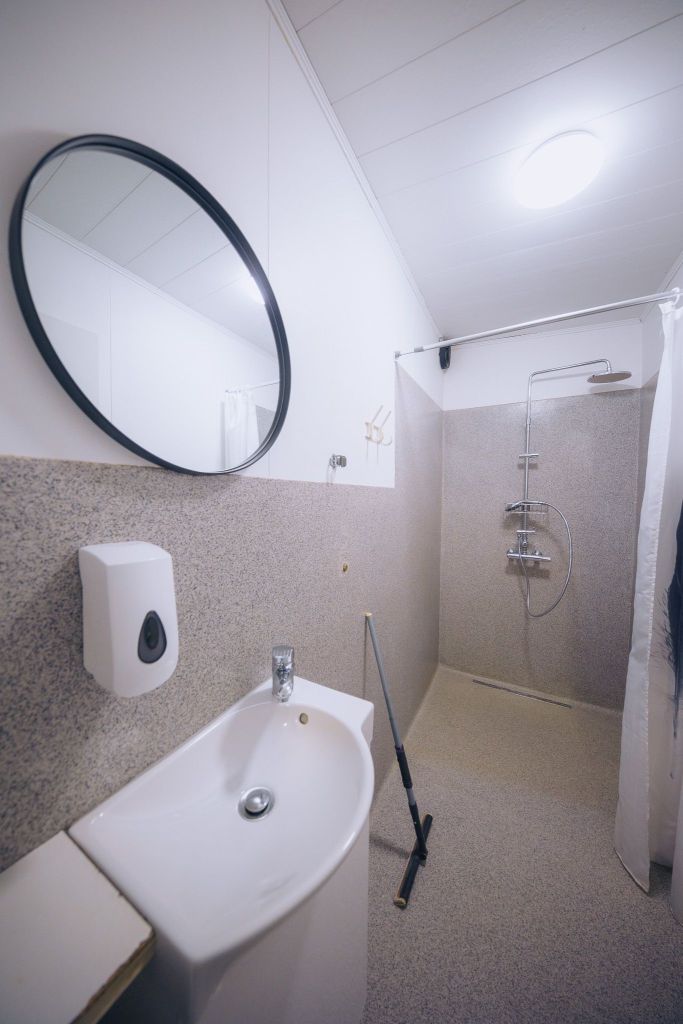 A modern bathroom with a round mirror, white sink, soap dispenser, and a walk-in shower with chrome fixtures.