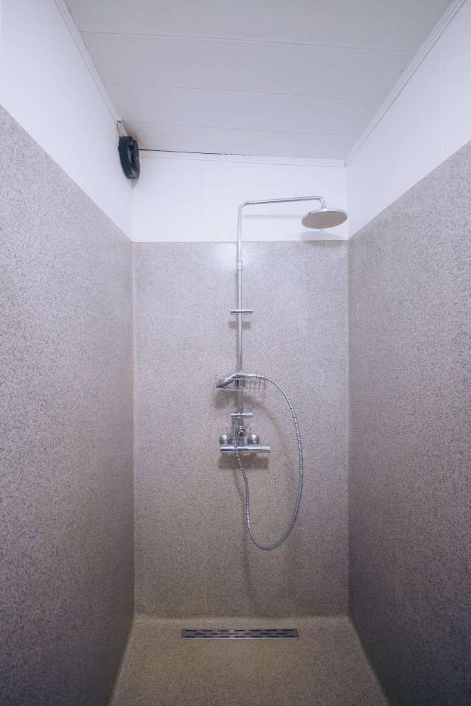 Minimalist shower with gray speckled walls, a sleek chrome showerhead, and a hose attachment.
