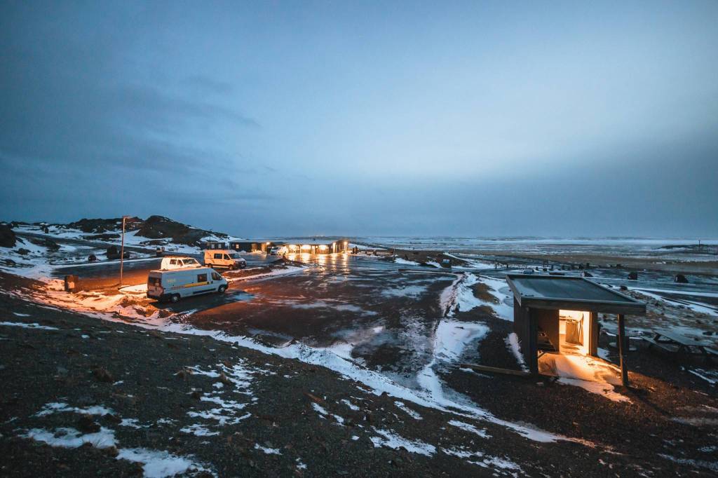 Remote icy landscape at dusk, lit buildings and vehicles contrast against the snowy terrain.