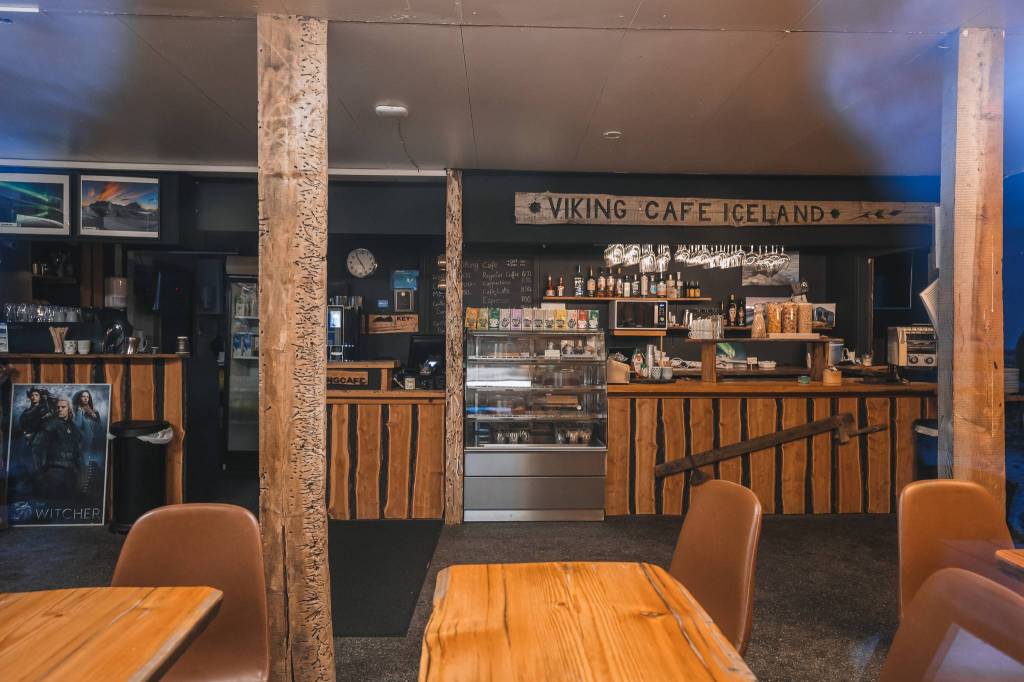 Cozy interior of Viking Cafe Iceland with wooden decor. A counter displays drinks and pastries. Tables and chairs in the front.