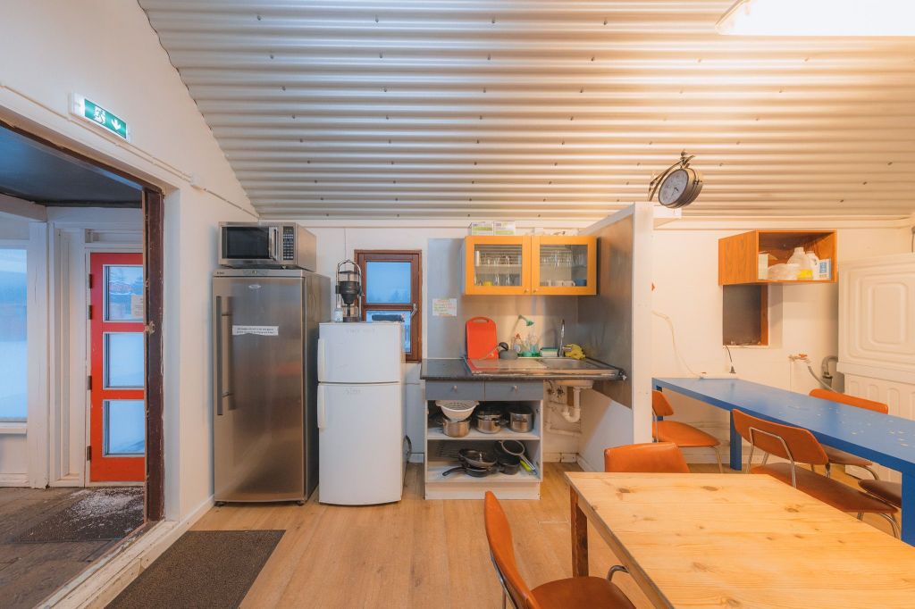 Cozy kitchen with a corrugated metal ceiling, wooden table, orange chairs, fridge, microwave, and wall clock.