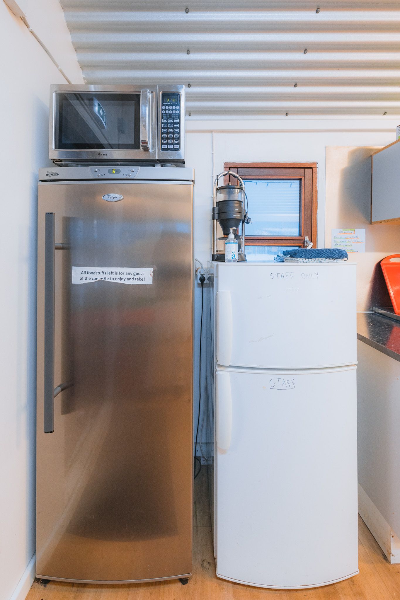 Two refrigerators are side by side in a small kitchen, a stainless steel fridge with a sign and a white one labeled "staff only," with a microwave on top.