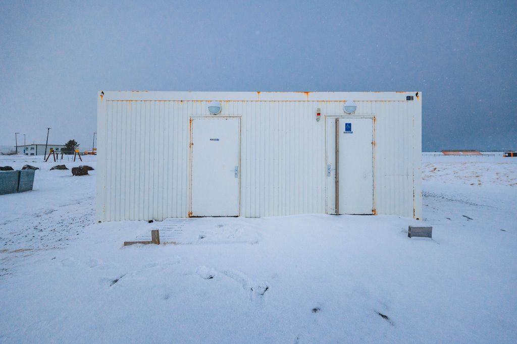 Small white building with two doors labeled "Women" and "Men," surrounded by snow under a gray sky.