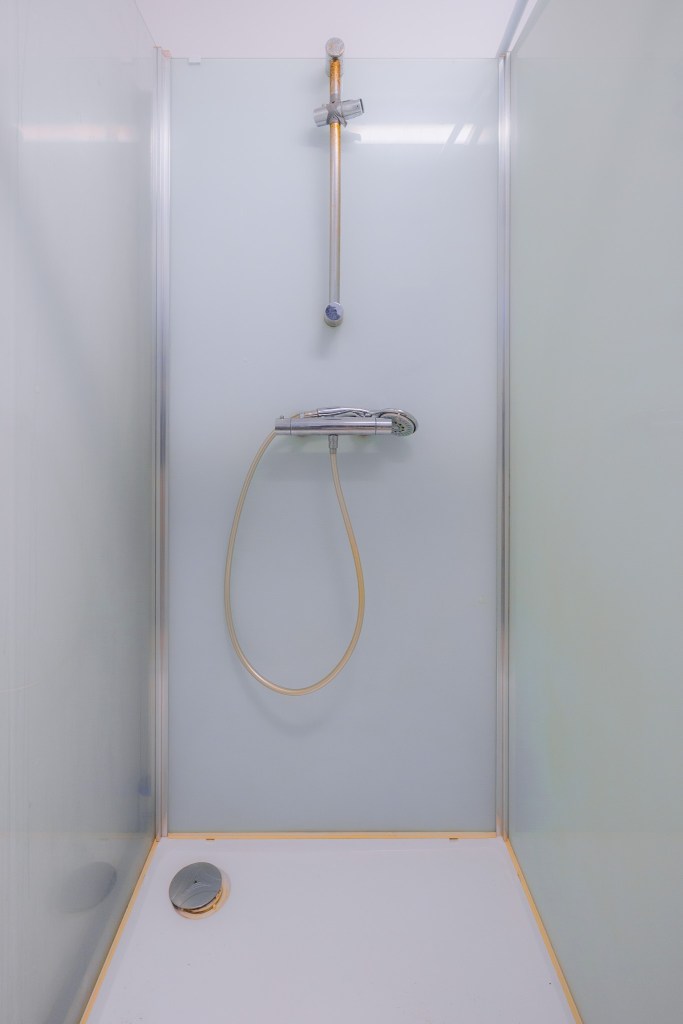 Minimalist shower with a glass door, overhead showerhead, and handheld attachment.