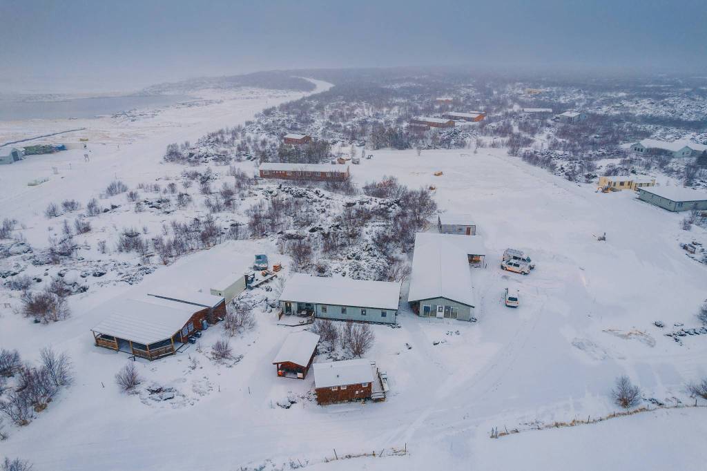 Aerial view of a snowy landscape with scattered buildings and trees. Overcast sky and distant waterway.